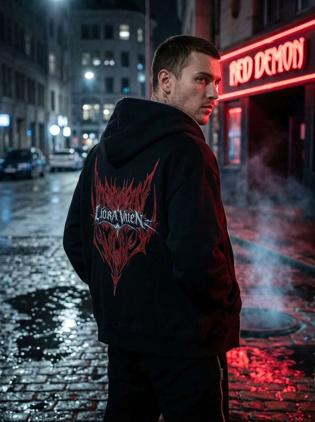Person wearing a black hoodie with red and white design on a city street at night.